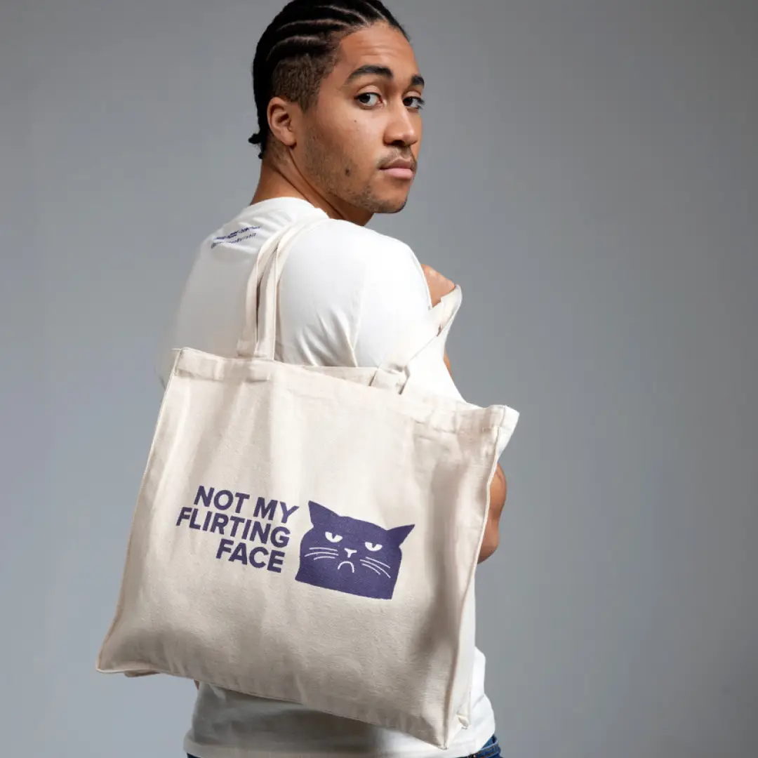 Person mit wei&szlig;em Jutebeutel &uuml;ber der Schulter, darauf ein blaues Katzenmotiv mit dem Text &sbquo;Not my flirting face&lsquo;.